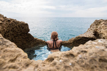 From above unrecognizable woman swimming at rocky landscape of natural pool located near cave near sea on sunny day in Algar seco caves in Algarve, Portugal - ADSF20891