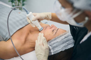 Professioneller Dermatologe wendet RF-Lifting-Gerät auf dem Gesicht einer reifen Frau während einer Hautpflege-Behandlung in einer Schönheitsklinik an - ADSF20913