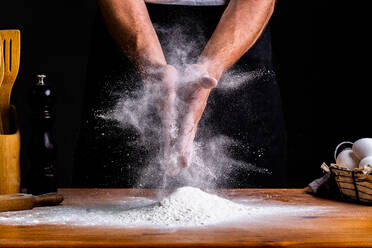 Faceless male baker clapping hands in flour while making bread dough with wheat flour and eggs at table - ADSF20922