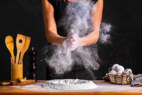 Gesichtslose Bäckerin klatscht bei der Herstellung von Brotteig mit Weizenmehl und Eiern am Tisch in die Hände - ADSF20927
