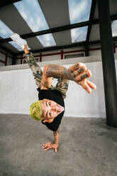 Ganzer Körper eines energischen jungen Mannes, der einen akrobatischen Handstand macht, während er einen Breakdance aufführt - ADSF20929