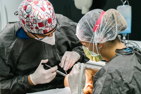 Professioneller Zahnarzt, der einem Patienten eine Betäubungsspritze verabreicht, während er mit einem Assistenten in einer modernen stomatologischen Klinik arbeitet - ADSF20933