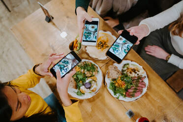 From above of diverse female friends gathering at table and taking photos of food on smartphones for social media - ADSF20983