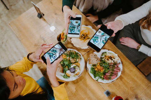 Von oben: Verschiedene Freundinnen versammeln sich am Tisch und fotografieren das Essen mit ihren Smartphones für die sozialen Medien - ADSF20983