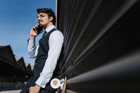 Männlicher Unternehmer schaut weg, während er mit seinem Smartphone gegen eine schwarze Wand spricht - EGAF01777