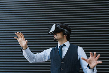 Male entrepreneur gesturing while watching movie through virtual reality simulator against wall - EGAF01782