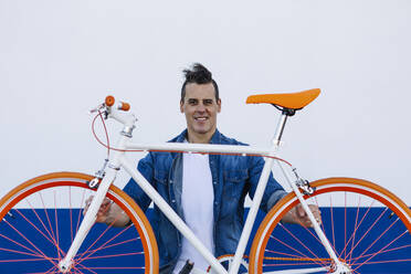 Lächelnder gut aussehender Mann mit orangefarbenem Fahrrad vor weißer Wand - XLGF01199