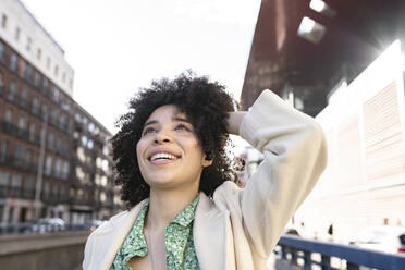 Lächelnde Afro-Frau mit Hand im Haar auf der Straße an einem sonnigen Tag - JCCMF01214