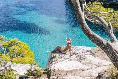 Woman sitting on rock by sea during sunny day - DGOF01984