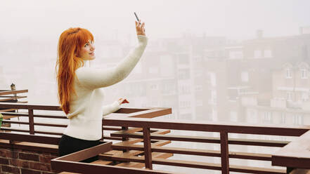 Lächelnde Frau nimmt Selfie durch Handy auf Terrasse - LJF02034