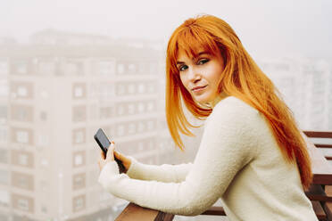 Beautiful woman holding mobile phone while leaning on railing - LJF02035