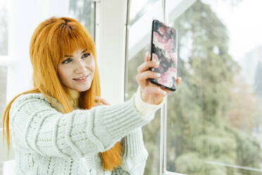 Lächelnde schöne Frau nimmt Selfie durch Fenster - LJF02051