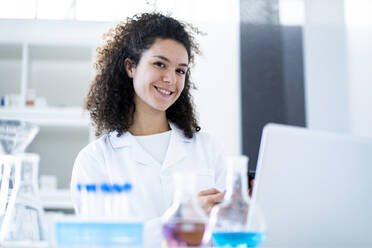 Lächelnde Ärztin mit Laptop im Chemielabor - GIOF11236