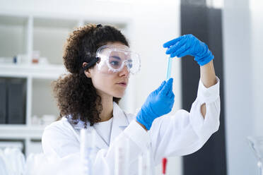Junge Wissenschaftlerin, die ein Reagenzglas im Chemielabor untersucht - GIOF11244