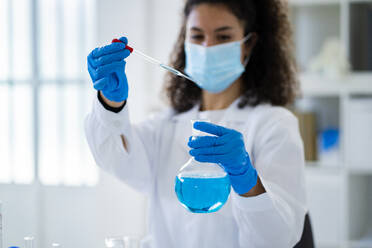 Young female doctor testing chemical solution in hospital during pandemic - GIOF11261