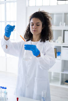 Female doctor mixing chemical solution in beaker through pipette at clinic - GIOF11275