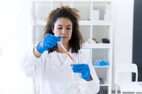 Young female scientist experimenting with chemical solution in beaker at hospital - GIOF11276