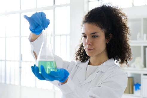 Young female doctor holding beaker with solution at chemistry lab - GIOF11283