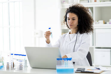 Wissenschaftlerin mit Reagenzglas bei der Arbeit am Laptop in einer Klinik - GIOF11295