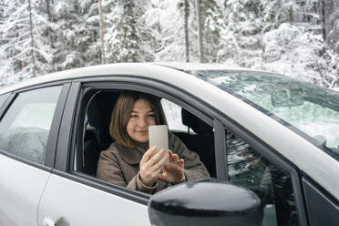 Young woman photographing through mobile phone while sitting in car - VPIF03516