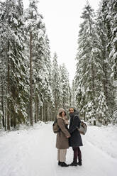 Paar mit Rucksack hält sich an den Händen, während es im Winter im Wald steht - VPIF03521