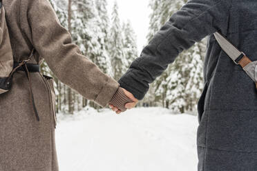Paar in warmer Kleidung hält sich an den Händen, während es im Wald steht - VPIF03522