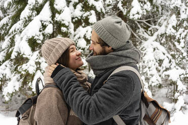 Couple wearing warm clothing looking at each other while standing in forest - VPIF03525