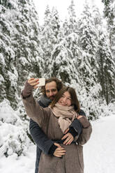 Freundin nimmt Selfie durch Handy mit Mann umarmt sie von hinten beim Stehen im Wald - VPIF03534