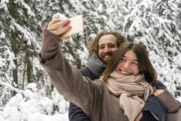 Lächelnde Frau, die ein Selfie mit einem Mann durch ein Mobiltelefon macht, während sie im Wald steht - VPIF03535