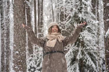 Smiling woman stretching hand while standing in forest - VPIF03545