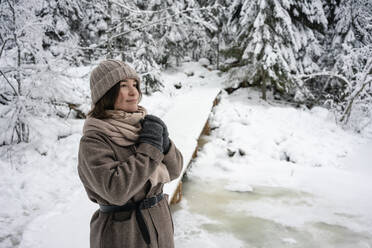 Young woman wearing warm clothing looking away while standing in forest - VPIF03571