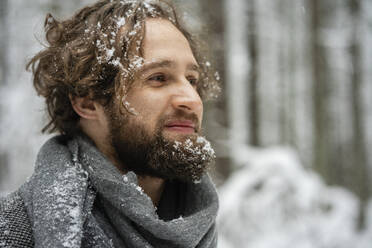 Smiling man with hair and beard covered with snow looking away while standing in forest - VPIF03575