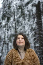 Junge Frau mit Pullover, die im Wald steht und nach oben schaut - VPIF03579