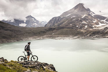 Mountainbiker mit Blick auf den Griessee, stehend am Nufenenpass, Wallis, Schweiz - MSUF00503