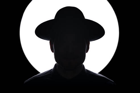 Silhouette eines Mannes mit Hut, der vor einer beleuchteten Lichtanlage steht - MSUF00504