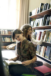 Studentinnen lesen Bücher, während sie in der Bibliothek sitzen - AJOF01053
