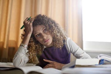 Thoughtful woman sitting at desk with books in library - AJOF01055