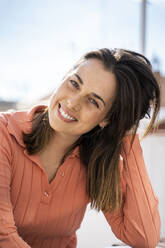 Junge Frau mit Hand im Haar lächelnd auf der Terrasse sitzend - AFVF08161