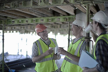 Lächelnde Bauarbeiter, die auf der Baustelle diskutieren - AJOF01060