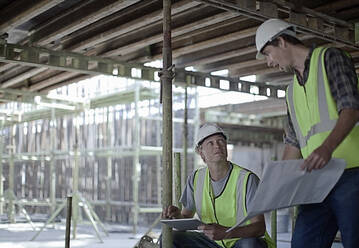 Male construction workers holding digital tablet while planning with coworker at construction site - AJOF01061