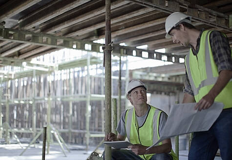 Männliche Bauarbeiter halten ein digitales Tablet, während sie mit einem Kollegen auf der Baustelle planen - AJOF01061