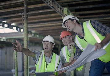 Male construction worker pointing while discussing with coworkers over blueprint at construction site - AJOF01062