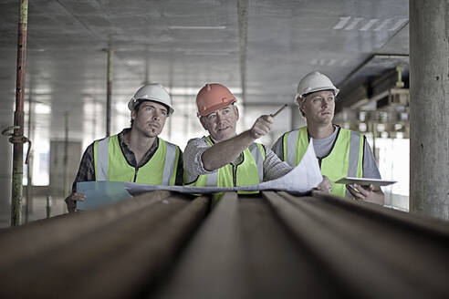 Männlicher Bauarbeiter bespricht mit Kollegen auf der Baustelle einen Plan - AJOF01064