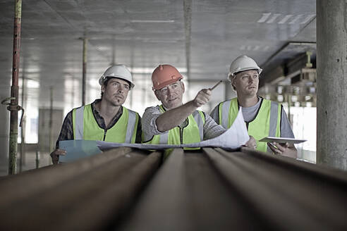 Male construction worker discussing plan with coworkers at construction site - AJOF01064