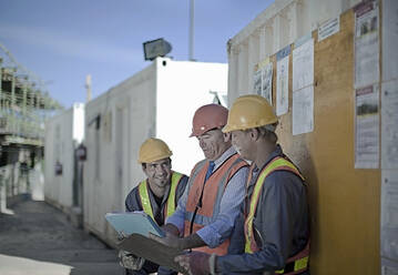 Lächelnde männliche Bauarbeiter, die auf einer Baustelle diskutieren - AJOF01070