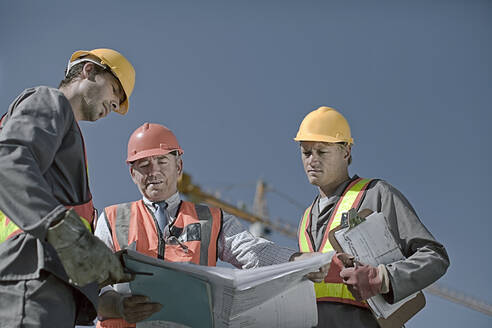 Männlicher Bauarbeiter diskutiert mit Kollegen auf der Baustelle gegen den klaren Himmel - AJOF01071