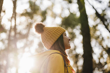 Smiling woman in knit hat looking away in forest - EBBF02475