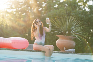 Lächelnde Frau in Badekleidung, die ein Selfie mit ihrem Handy am Pool macht - AKLF00068