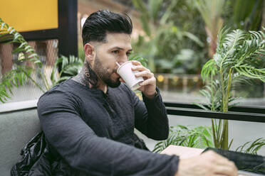 Tätowierter Hipster-Mann trinkt Kaffee im Laden - JCCMF01247