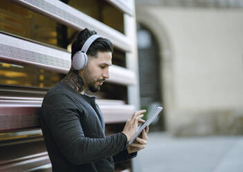 Handsome man with headphones using digital tablet against metal wall - JCCMF01249